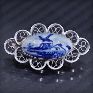 May include: A silver filigree brooch with a blue and white porcelain cameo featuring a windmill scene.