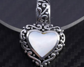 Op de afbeelding: Een zilveren hartvormige hanger met een witte parelmoer inleg en een ingewikkeld scrollwerk ontwerp.