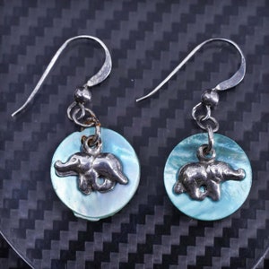Può includere: Un paio di orecchini d'argento con ciondoli a forma di conchiglia blu e bianca con un design di elefante d'argento.
