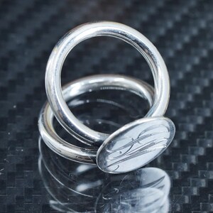 May include: A silver ring with a round, engraved design. The ring is made of two interlocking bands.