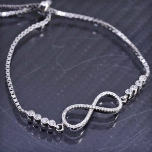 May include: A silver bracelet with an infinity symbol, embellished with small, clear gemstones. The bracelet has a fine chain design with additional gemstones set along the sides, creating a sparkling accessory.