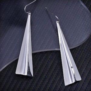 May include: A pair of silver dangle earrings with a triangular shape. The earrings are made of a smooth, shiny metal.