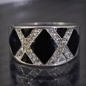 Puede incluir: Un anillo de plata con esmalte negro y diamantes de imitación transparentes dispuestos en un patrón geométrico.