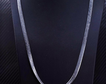 Puede incluir: Un collar de cadena de serpiente plateado sobre un fondo negro.