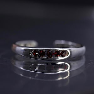May include: A silver-toned cuff bracelet with five round, deep red gemstones set in a row. The bracelet has an open design, allowing it to be adjusted. The gemstones are evenly spaced and add a pop of color to the polished metal.
