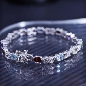 May include: A silver bracelet with a variety of colorful gemstones, including blue, green, red, and purple. The bracelet has a clasp closure.