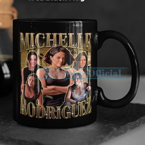 Puede incluir: Taza de cerámica negra con un diseño dorado que presenta el texto "Michelle Rodriguez" y un collage de imágenes de la actriz. La taza tiene una capacidad de 310 ml.