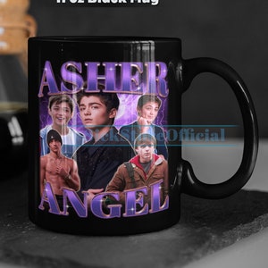 May include: Black 11 oz mug featuring a collage of images and the name "ASHER ANGEL" in purple text. The mug has a black handle and a black interior. The text "11 oz Black Mug" is printed at the top of the mug.