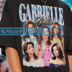 Puede incluir: Camiseta negra unisex con la palabra "GABRIELLE", el nombre "Solis" e imágenes de mujeres. La camiseta también tiene el texto "SickStoreOfficial". La modelo lleva una camiseta 2XL.