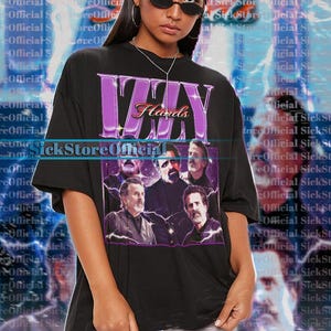 May include: Black unisex t-shirt featuring a graphic of a band with the text "Izzy Hards" in purple. The shirt also has the text "SickStoreOfficial". The model is wearing a 2XL shirt.