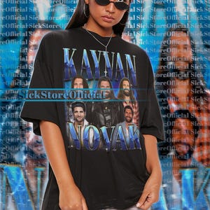 Peut inclure: T-shirt noir unisexe avec l'inscription "KAYVAN NOVAK" et un graphisme de six hommes. Le t-shirt a un aspect vintage et vieilli. Le modèle porte une taille 2XL.