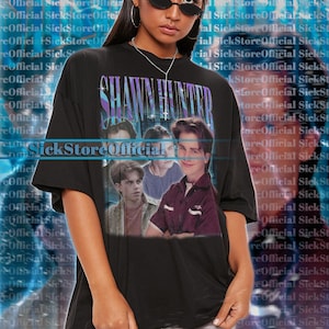 Könnte beinhalten: Schwarzes Unisex-T-Shirt mit einer Grafik von Shawn Hunter aus der Fernsehserie Boy Meets World. Das Design hat einen Vintage-Stil mit dem Text "Shawn Hunter" in Lila und Blau. Das Model trägt ein 2XL-Shirt.