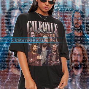 Puede incluir: Camiseta unisex negra con un gráfico de la palabra "GILEFOYLE" y un collage de hombres. La camiseta tiene mangas cortas y cuello redondo. La modelo lleva una talla 2XL.