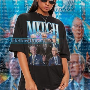 Könnte beinhalten: Schwarzes Unisex-T-Shirt mit einer Grafik von Mitch McConnell und dem Text "Mitch McConnell". Das Shirt hat einen Vintage-Stil mit Blitzakzenten und einem verblichenen Look. Das Model trägt ein 2XL-Shirt.