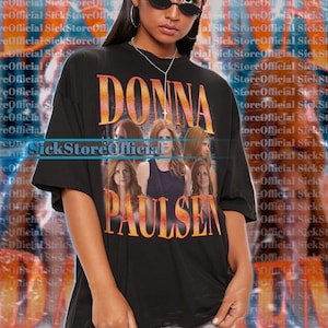 May include: Black unisex t-shirt featuring the text "DONNA PAULSEN" in orange and yellow lettering. The shirt has a graphic of several women. The text "SickStoreOfficial" is also visible.