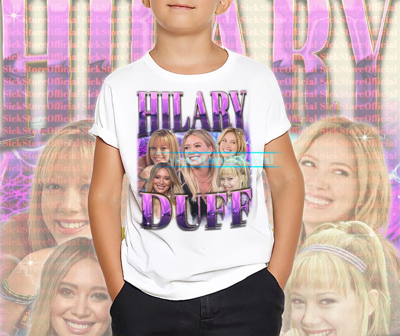 May include: White t-shirt featuring a graphic of Hilary Duff in a purple and white design. The shirt has the text "HILARY DUFF" in a retro font. The background has a repeating pattern of the text "SickStoreOfficial".