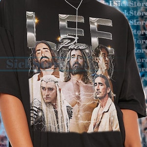 Könnte beinhalten: Schwarzes T-Shirt mit einer Grafik von mehreren Männern mit langen Haaren und dem Text "LEE Pace" in metallischem Silber. Das Shirt hat einen Rundhalsausschnitt und kurze Ärmel. Das Model trägt Größe 2XL.