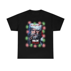 May include: Black t-shirt with a graphic of a man dressed as Santa Claus with a beard and a candy cane in his mouth. The graphic is surrounded by red and green Christmas lights. The text "You better be good" and "Violent Night" is on the graphic.