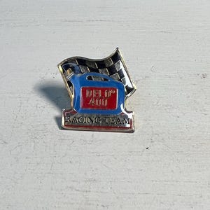 May include: A gold-colored pin with a blue oil can and a checkered flag. The oil can has the text "Del. 0" and "4000" on it. The pin also has the text "Racing Team" on it.
