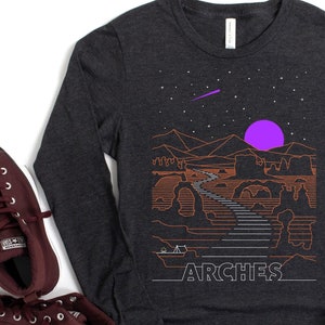 May include: A dark gray long-sleeve t-shirt with a graphic design of a desert landscape with a purple moon and the word "ARCHES" printed in white.