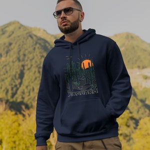 May include: A navy blue hooded sweatshirt with a graphic of a desert landscape featuring cacti and a setting sun. The text "SAGUARO" is printed below the graphic.