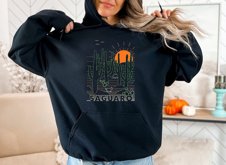 May include: Black hooded sweatshirt with a graphic print of a desert landscape with cacti and a setting sun. The text "SAGUARO" is printed below the graphic.