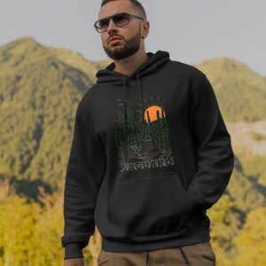 May include: Black hooded sweatshirt with a graphic print of a desert landscape with cacti and a setting sun. The text "SAGUARO" is printed below the graphic.