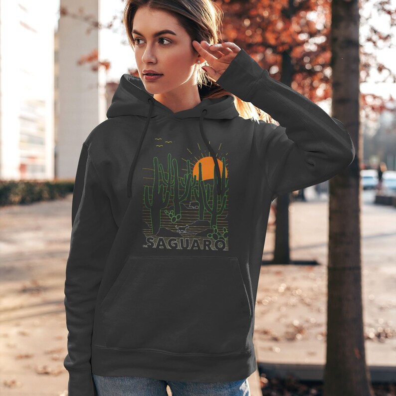 May include: A dark gray hooded sweatshirt with a graphic print of a desert landscape featuring cacti, a setting sun, and the word "SAGUARO" in green text.