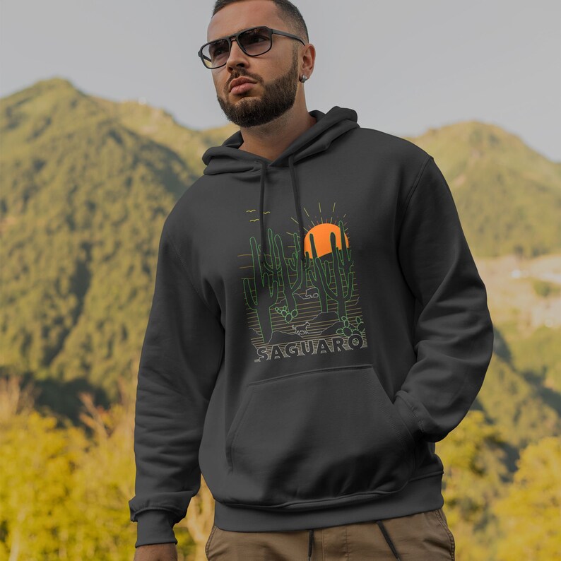 May include: A dark gray hooded sweatshirt with a graphic print of a desert landscape featuring saguaro cacti, a setting sun, and the word "SAGUARO" in orange.