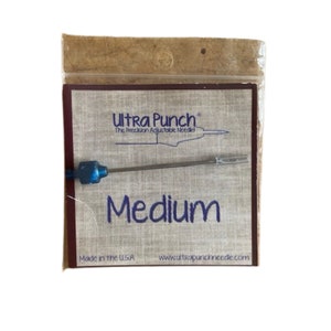 May include: A close-up of a silver Ultra Punch needle with a blue handle. The needle is packaged in a brown paper bag with the text "Ultra Punch" and "The Precision Adjustable Needle" printed on it. The size of the needle is "Medium". The text "Made in the USA" and "www.ultrapunchneedle.com" are printed on the bottom of the bag.