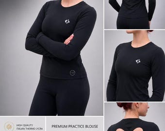 Può includere: Una blusa da allenamento nera a maniche lunghe con scollo rotondo, un piccolo logo bianco sul petto e un'apertura a forma di cuore sulla schiena con spalline incrociate. Il testo MNi PREMIUM PRACTICE BLOUSE è chiaramente visibile.