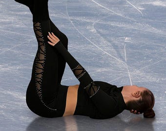 Könnte beinhalten: Eine Eiskunstläuferin in schwarzem Outfit führt eine Bewegung auf dem Eis aus. Die Läuferin ist kopfüber mit ausgestreckten Beinen, trägt schwarze Leggings mit Schnürdetails. Die Kufen der Eislaufschuhe sind sichtbar.