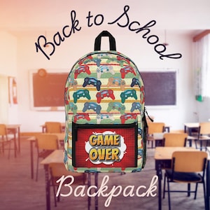 Op de afbeelding: Een rugzak met een patroon van kleurrijke videogamecontrollers op een gestreepte achtergrond. De voorzak heeft een "Game Over" afbeelding. De woorden "Back to School" en "Backpack" staan op de afbeelding.