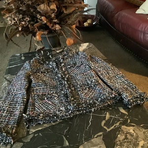 May include: A blue, black, and white tweed jacket with a frayed hem and a button closure.