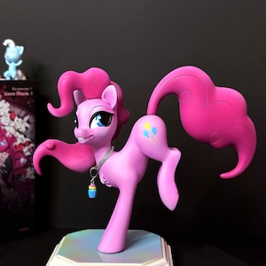 Puede incluir: Figura de My Little Pony rosa con un amuleto de cupcake azul, de pie sobre una base blanca con el texto "Mystical World of Creatures".