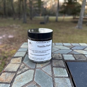 May include: A small glass jar with a black lid and a white label that reads "Crenshaw farms Vanilla Paste Made with organic vanilla beans, American vodka, brown sugar, honey and xanthan gum https://crenshawfarms.etsy.com This is a cottage food operation that is not subject to Florida safety regulations 5.2 oz"