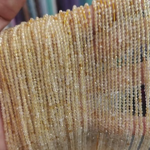 Peut inclure: Gros plan sur plusieurs brins de petites perles rondes jaune doré. Les perles sont enfilées ensemble, créant un aspect fluide et texturé. Ces perles sont probablement des pierres précieuses ou des cristaux, idéales pour la création de bijoux.