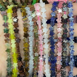 Puede incluir: Una hebra de cuentas de piedras preciosas en forma de estrella en varios colores, incluyendo verde, amarillo, marrón, blanco, rosa, azul y gris.