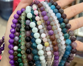 May include: A collection of 14 strands of gemstone beads, each strand featuring a different colour and type of stone. The beads are round and smooth, and the colours include purple, green, blue, brown, and white.