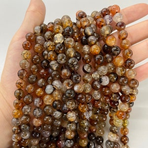May include: A strand of brown, orange, and white agate beads. The beads are round and have a natural, polished finish.