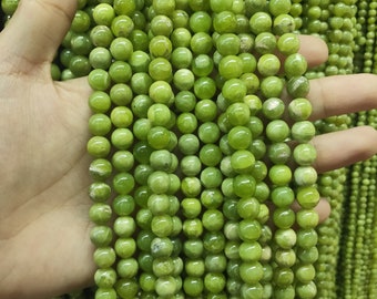 May include: A strand of green jade beads, each bead is round and smooth. The beads are strung on a clear thread and are displayed on a hand.