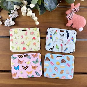 May include: Four square plastic badge holders with rounded corners and top slots. One features a yellow floral pattern, one a light blue bird print, one a light pink butterfly design, and one a light blue background with various dessert illustrations.