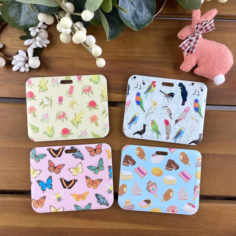 May include: Four square plastic badge holders with rounded corners and top slots. One features a yellow floral pattern, one a light blue bird print, one a light pink butterfly design, and one a light blue background with various dessert illustrations.