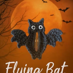 May include: A dark gray crochet bat hair clip with white eyes and a gold-colored clip. The image has the text "Crochet Pattern PDF" and "Flying Bat" on an orange background with a full moon and bats.