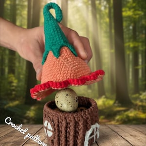 May include: A handmade crochet fairy house with a speckled egg inside. The house is brown with white window details. A matching crochet hat in orange, green, and red is held above the house. The text "CrochetPatterns85" and "Crochet pattern pdf" are visible.