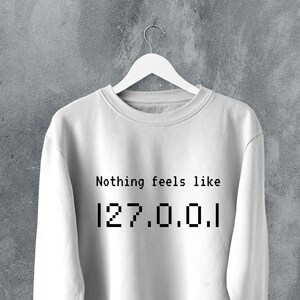 Peut inclure: Sweat-shirt blanc avec le texte "Nothing feels like 127.0.0.1" imprimé sur le devant.