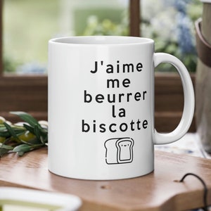 May include: White ceramic mug with black text that reads "J'aime me beurrer la biscotte" and a simple illustration of a slice of bread.