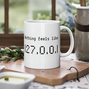 Può includere: Tazza in ceramica bianca con testo nero che recita "Nothing feels like 127.0.0.1".