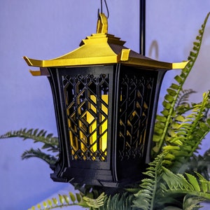 May include: A black and gold lantern with a geometric design. The lantern has a light inside, casting a warm glow.