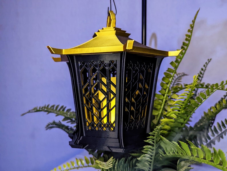May include: A black and gold lantern with a geometric design. The lantern has a light inside, casting a warm glow.